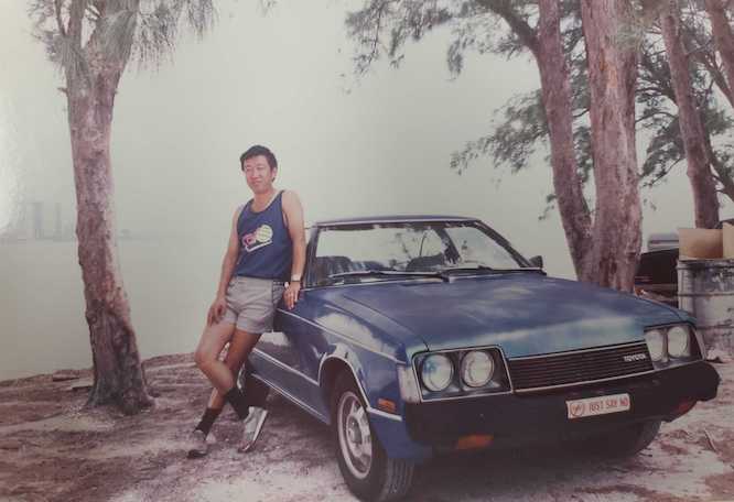 Finli CEO and founder Lori Shao's father stands next to his blue Toyota Corolla.